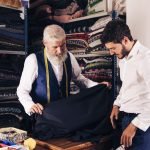 smiling-man-seller-displaying-blue-fabrics-young-customer-textile-shop